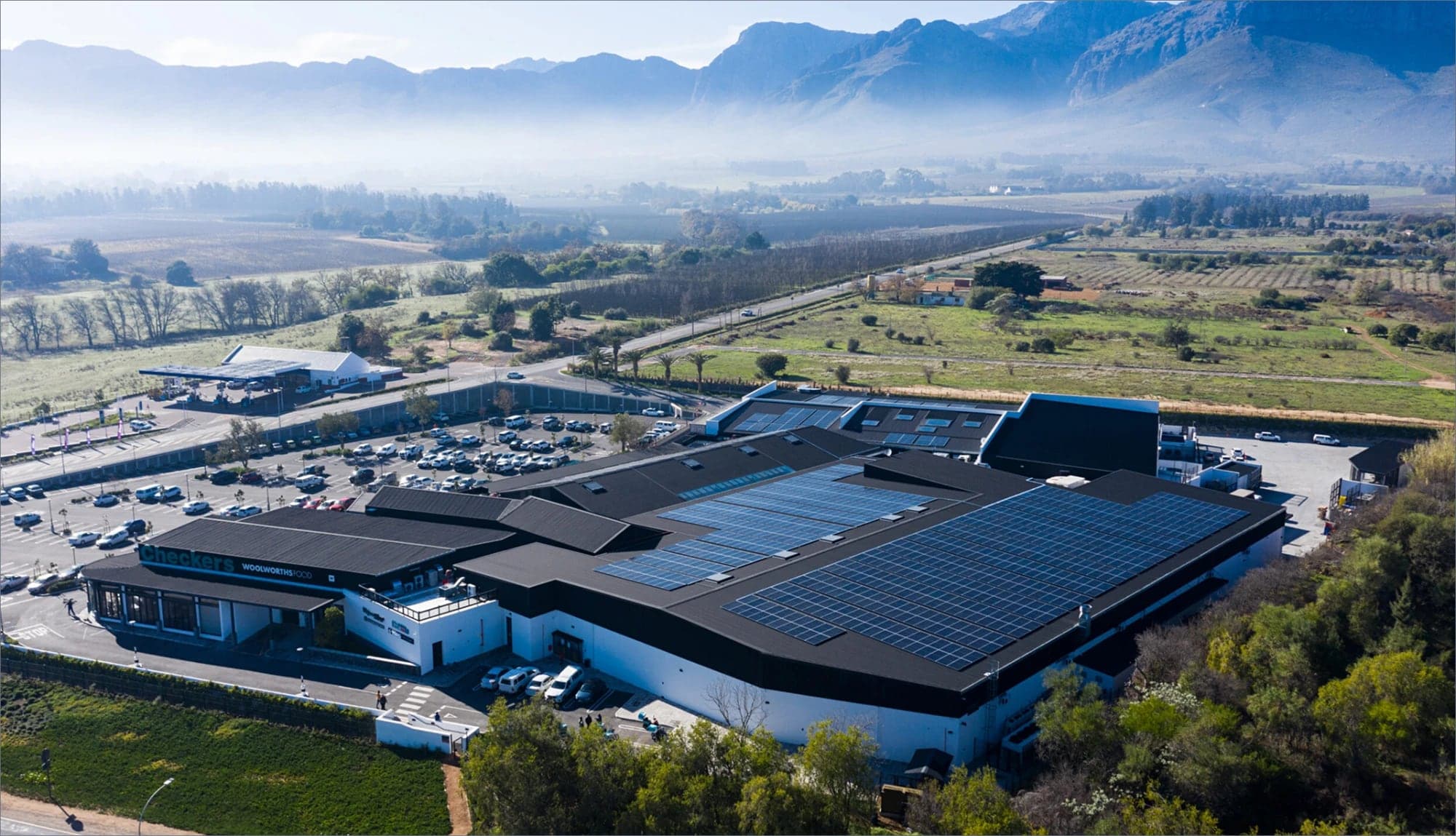 A shopping centre from the air, solar on the roof, mountains behind