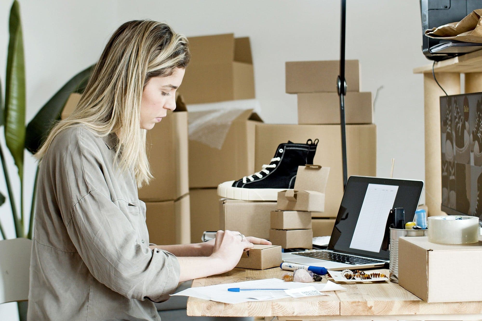 A shop owner packing orders at her desk, laptop open